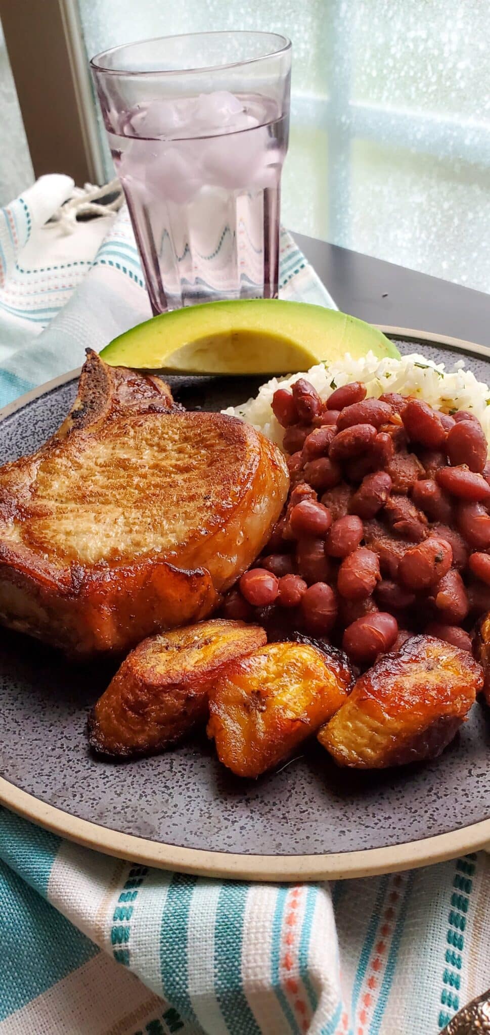 a plate of white rice, red beans, a pork chop, and fried plantains